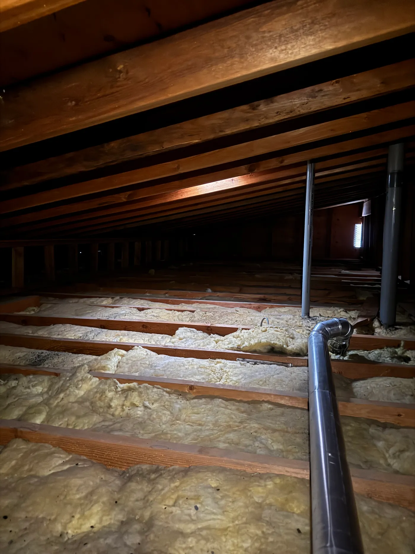 Under-insulated residential attic before a top-up, showing thin settled insulation between exposed floor joists with ductwork running through.