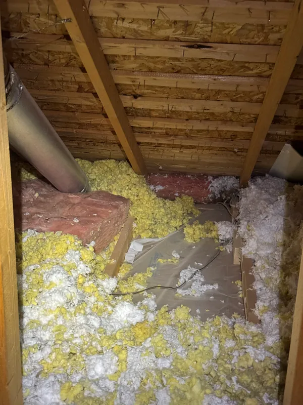 Attic floor with patchy insulation, yellow batt and white blown-in laid unevenly between the joists, with flexible duct and wiring running through it.