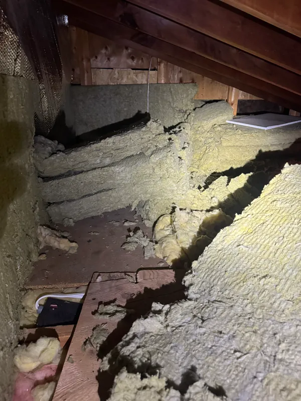 Attic with batt insulation sagging away from the framing, gaps along the edges and bare deck showing through underneath.