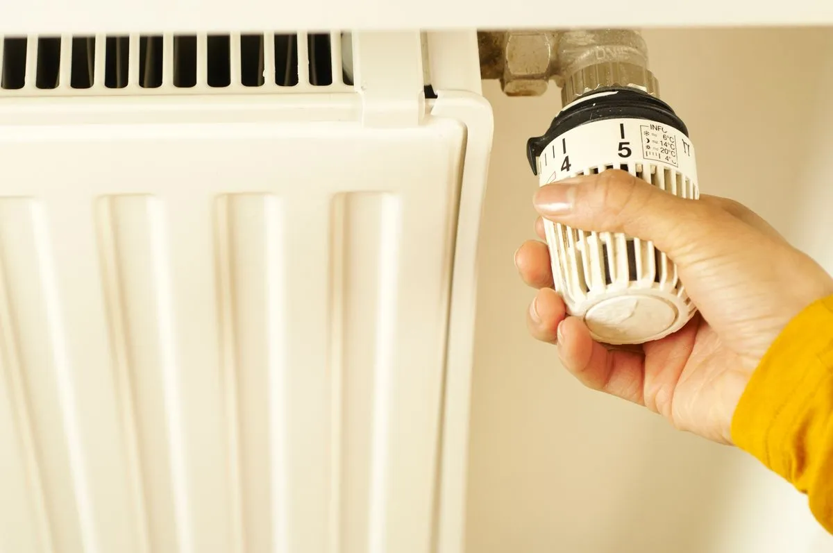 A hand turning down a home heating thermostat