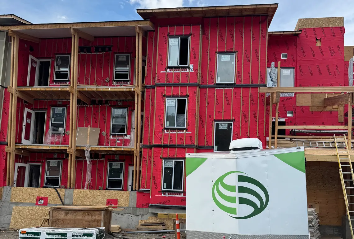 A three-storey wood-frame rental building in Kamloops BC wrapped in red weather membrane with the siding not yet started