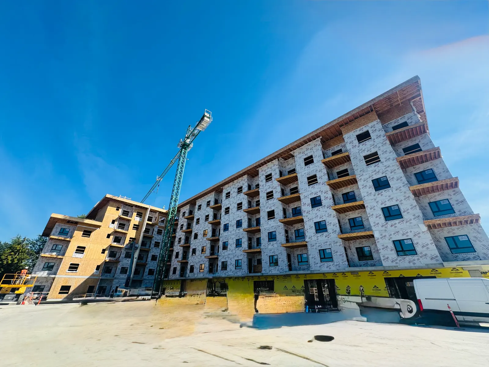 A six-storey wood-frame apartment building under construction in Maple Ridge BC with a tower crane alongside it