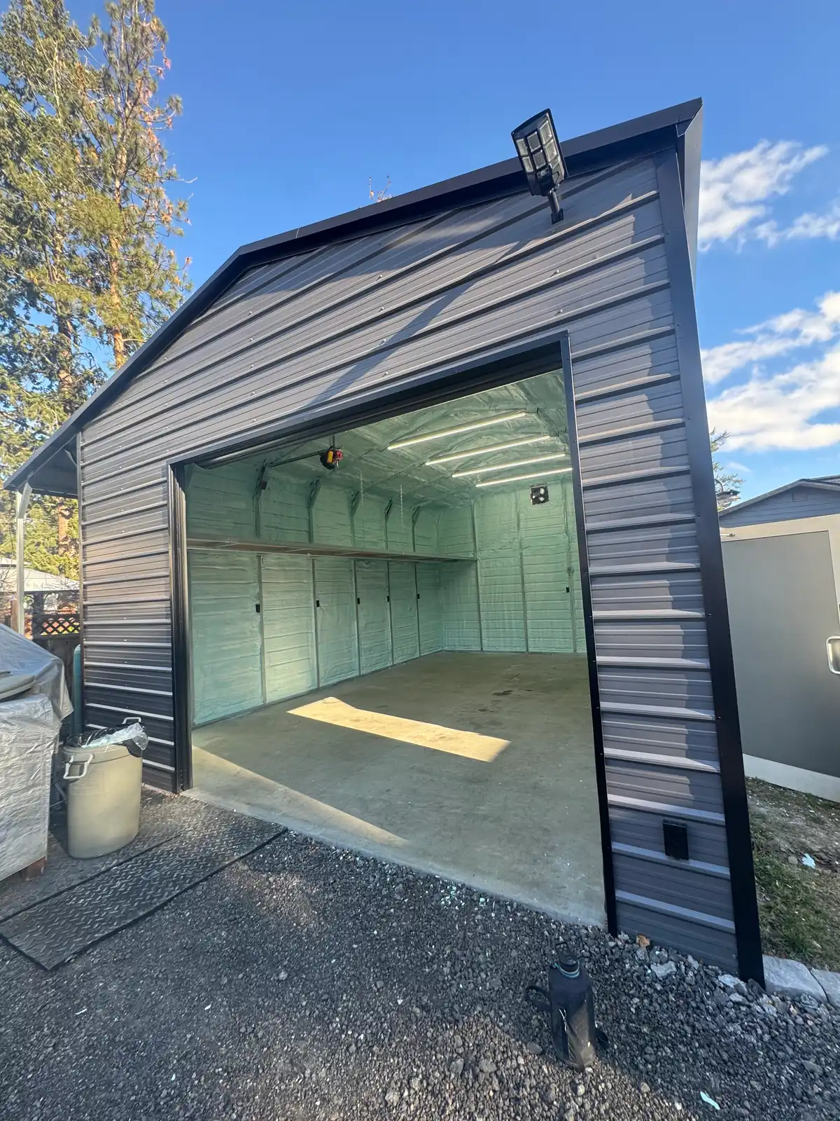 Finished black metal-clad garage with the green closed-cell spray foam interior visible through the open overhead door.