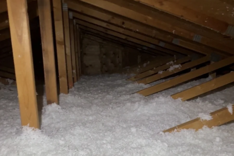 Attic after a blown-in top-up, even insulation covering the floor and running away between the trusses.