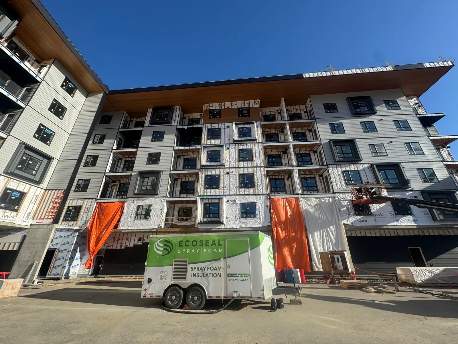 EcoSeal spray foam rig parked in front of a six-storey wood-frame MURB still in Tyvek and Protecto Wrap sheathing.